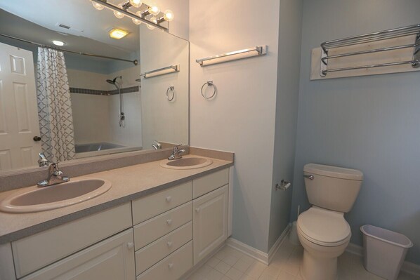 A bathroom with two sinks, a toilet, a shower, and a mirror with lights. - R Escape - 4 BR Semi-Oceanfront TownHome w/Community Pool access (Southern Shores)