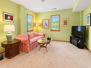 A living room with a sofa, a glass coffee table, a television, and framed artwork on the walls.