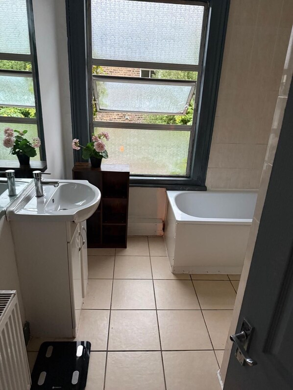 A bathroom with a white sink, a bathtub, and a window with a view of greenery.