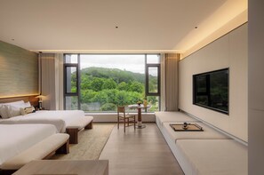 A modern hotel room with a large window offering a view of lush greenery. There are two beds, a desk, and a seating area with a flat-screen TV mounted on the wall. - Country Retreats-Guangzhou Bella vita manor (Guangzhou)