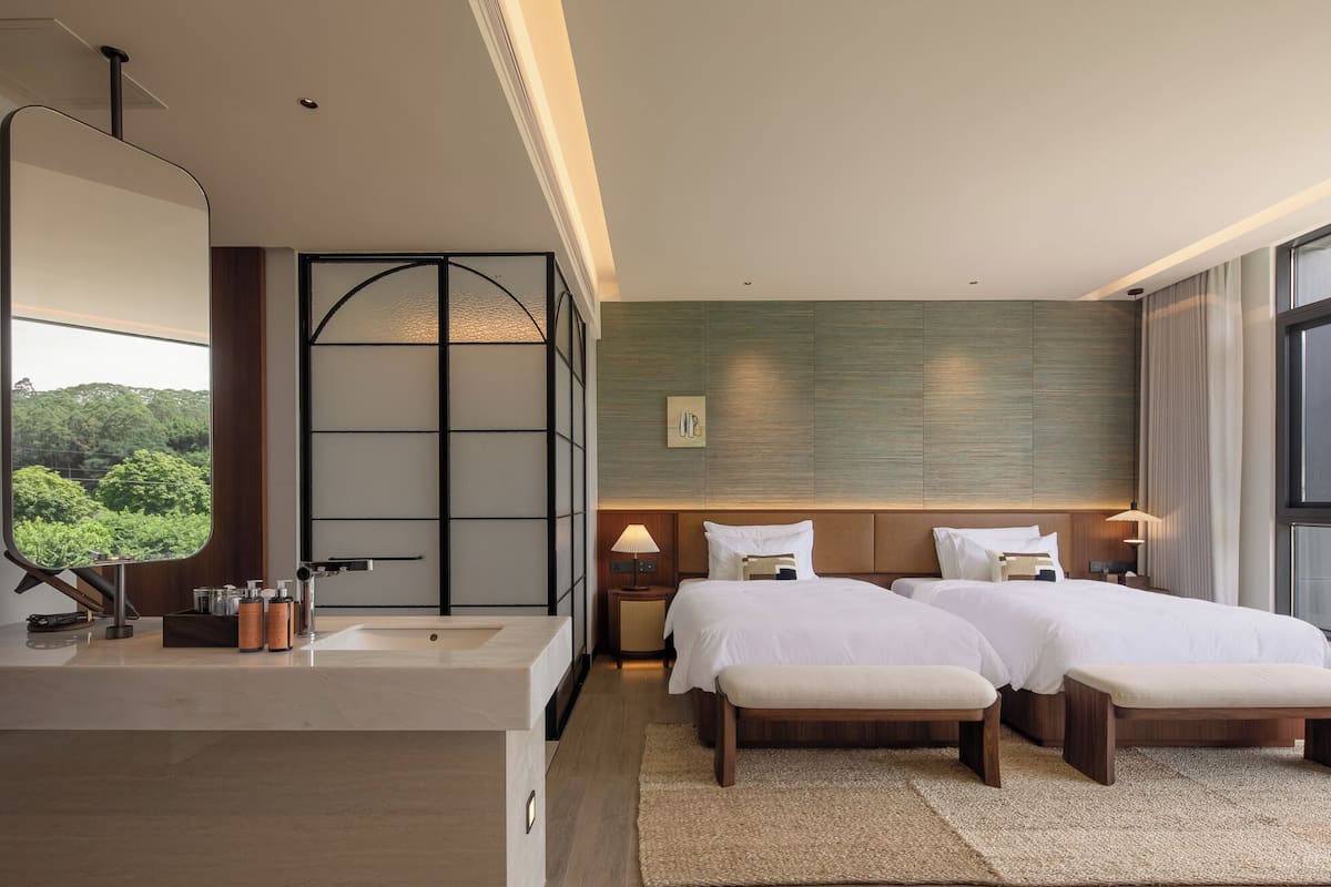 Een hotelkamer met een groot raam, een bed, een nachtkastje, een spiegel en een wastafel.