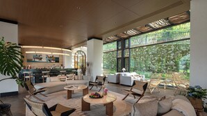 Un espacio interior amplio con un conjunto de asientos, una cocina y grandes ventanales con vistas a la vegetación.