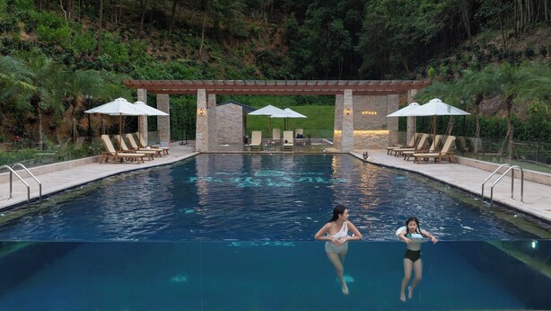 Una piscina con sillas de descanso y sombrillas, rodeada de vegetación.