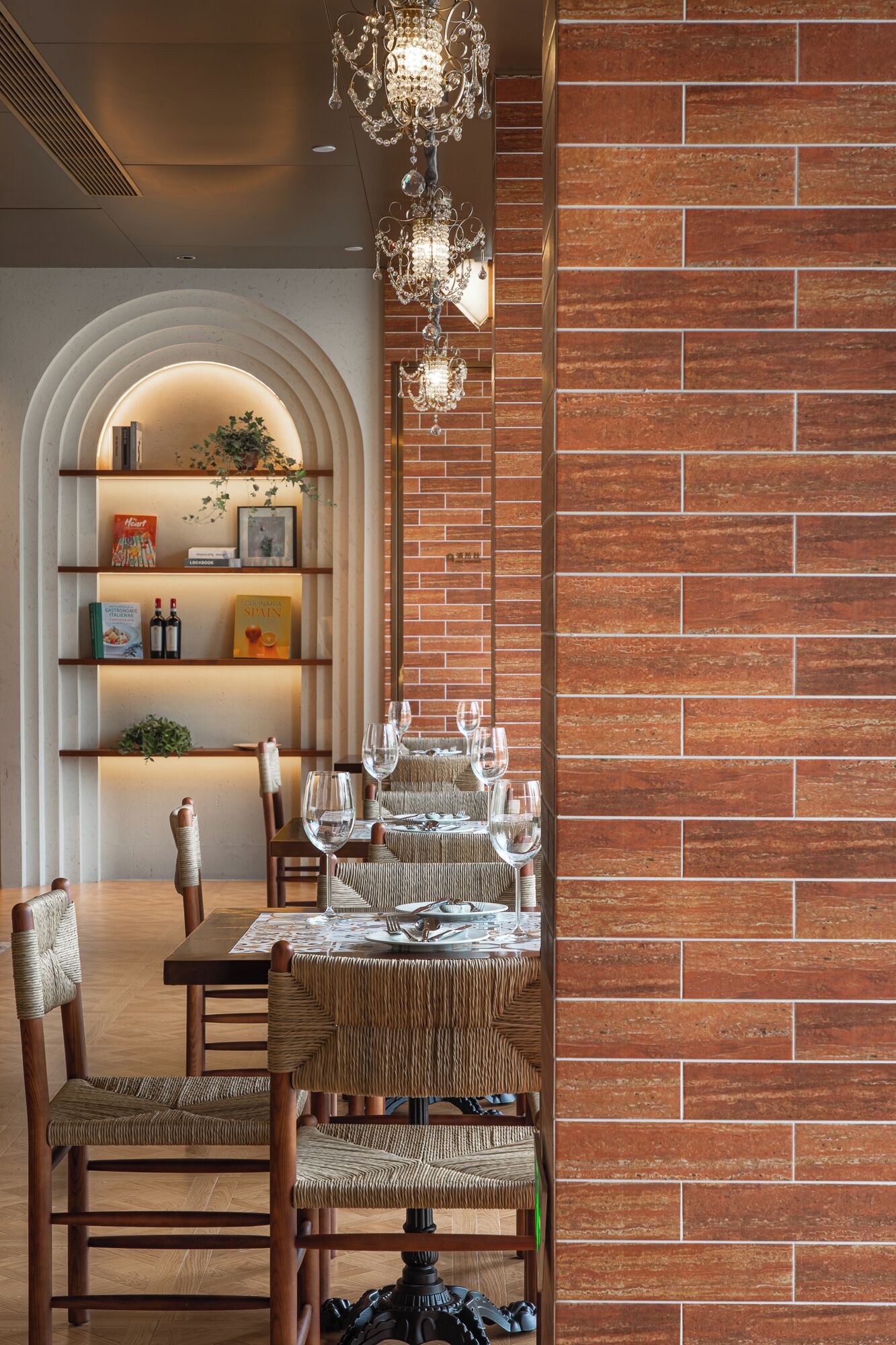 A dining area with a brick wall, a chandelier, and a bookshelf with books and decorative items.