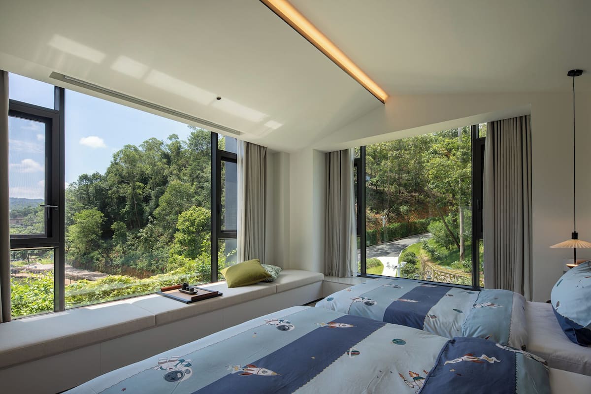 Een moderne slaapkamer met grote ramen, een inbouwbank en uitzicht op een weelderig landschap.