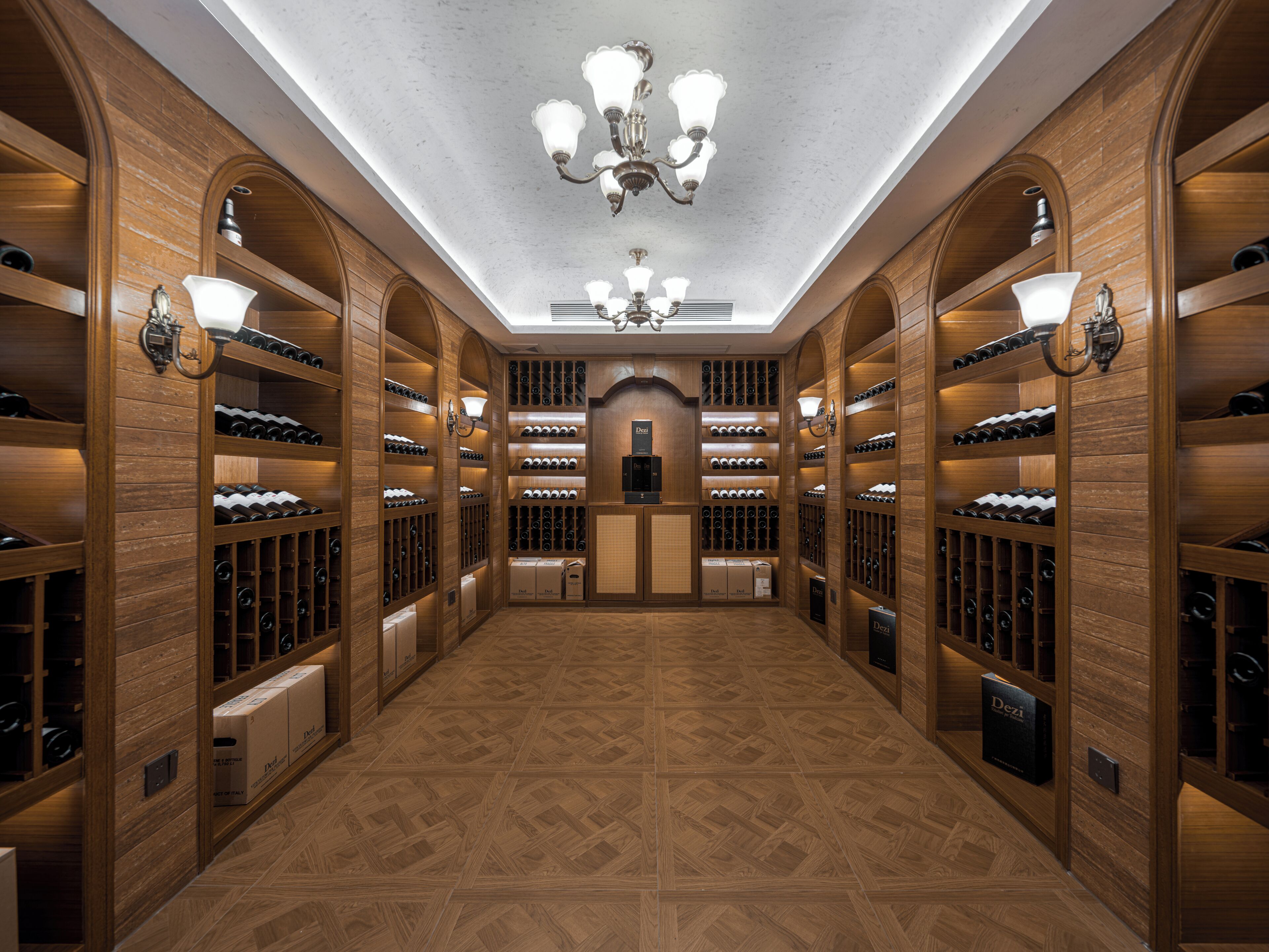 A wine cellar with wooden shelving, a central aisle, and a chandelier.