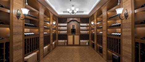 A wine cellar with wooden shelving, a central aisle, and a chandelier.