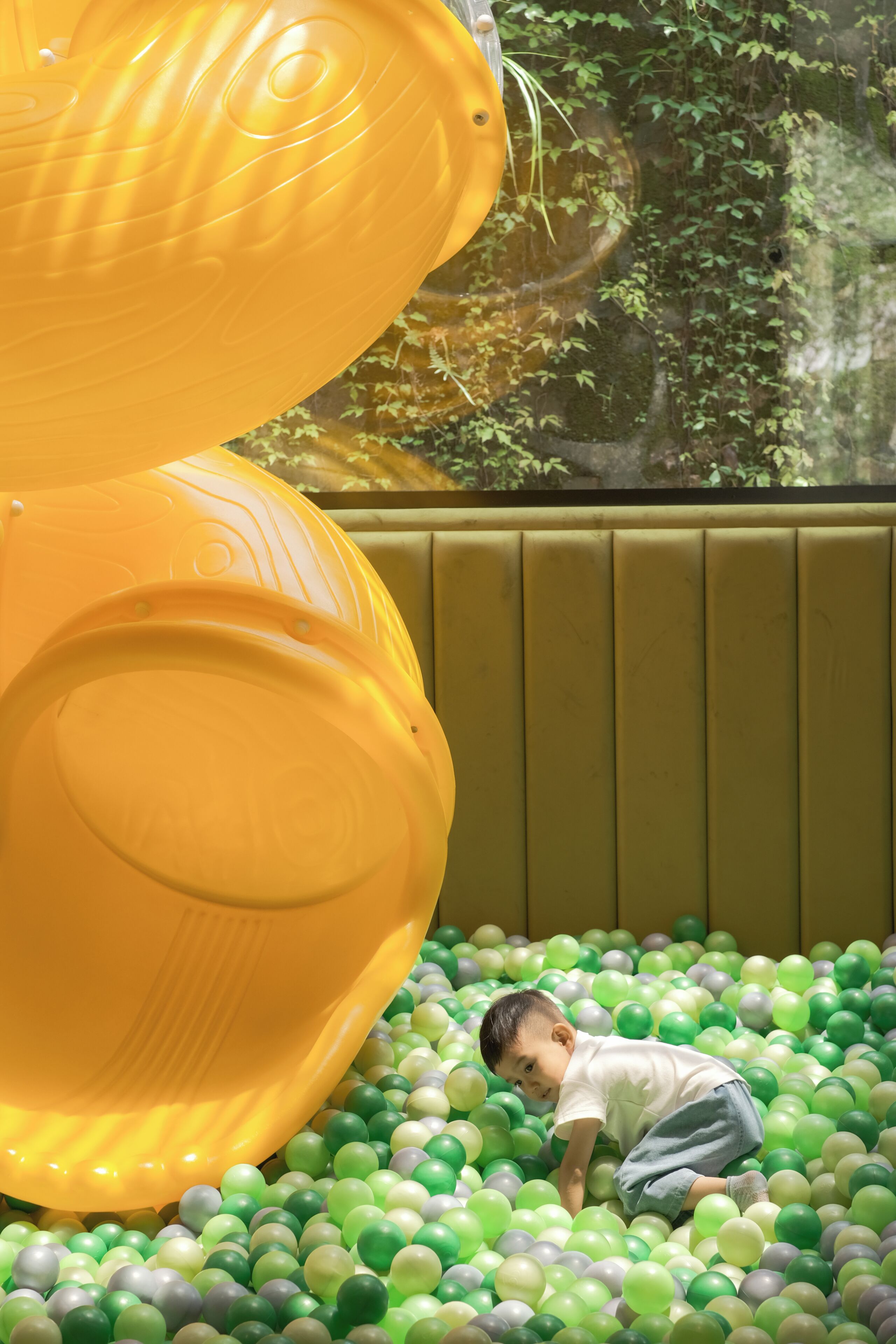 Niño jugando en una piscina de pelotas verdes y amarillas.