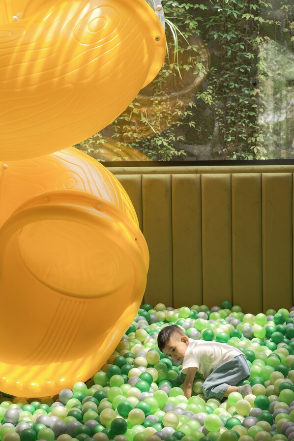 Niño jugando en una piscina de pelotas verdes y amarillas.