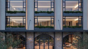 Un edificio moderno con tres ventanas arqueadas, una entrada central con puertas de cristal y un pequeño patio con una fuente.