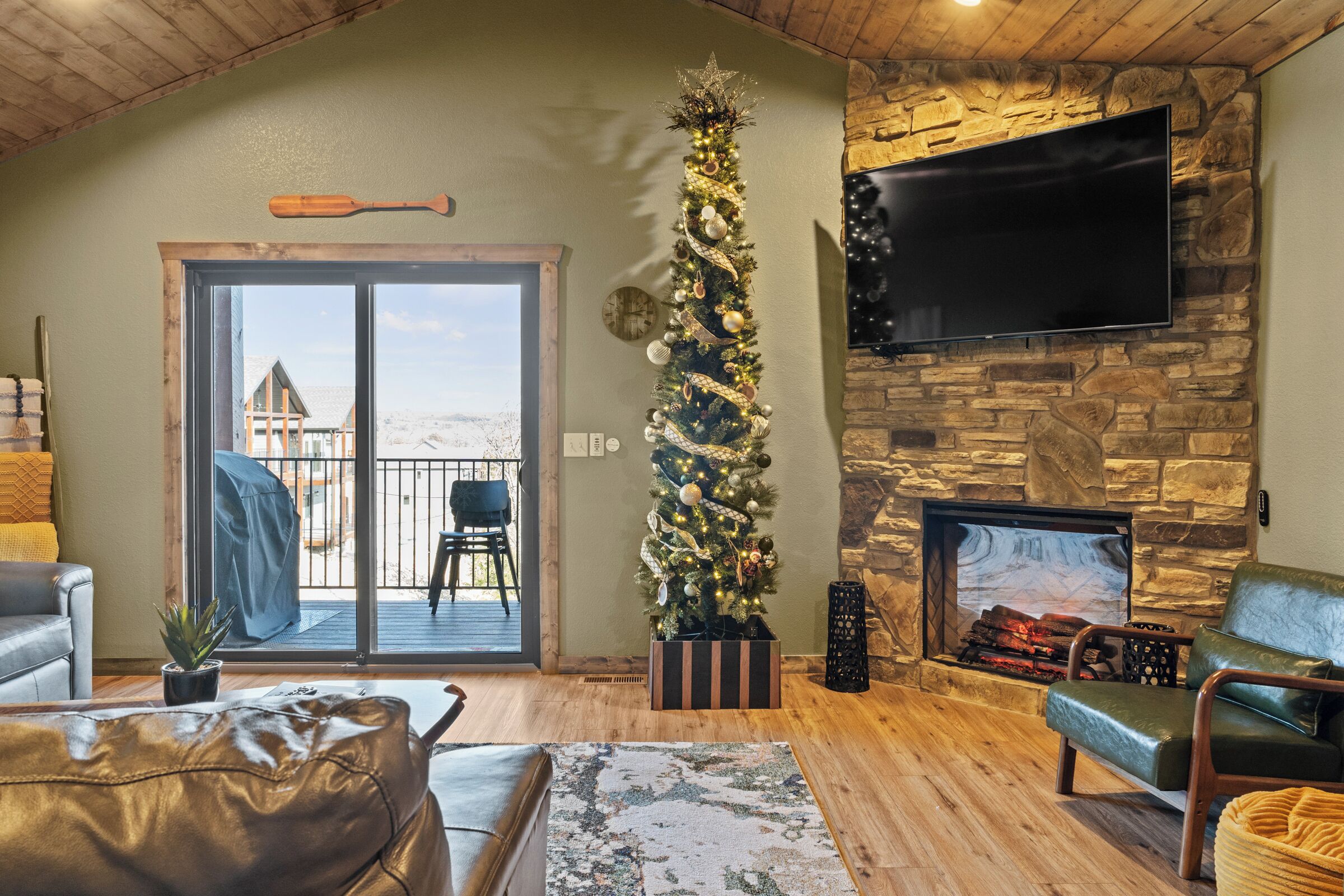 A cozy living room with a fireplace, a Christmas tree, and a large TV mounted on a stone wall.