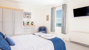 Ein Schlafzimmer mit Bett, Stuhl, Kleiderschrank, Schreibtisch und einem Fenster mit Vorhängen.