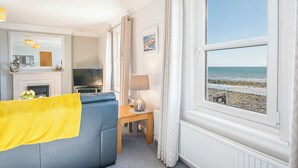 Ein Zimmer mit einer Couch, einem Fernseher, einem Kamin, einem Tisch mit einer Lampe und Blick auf den Strand.