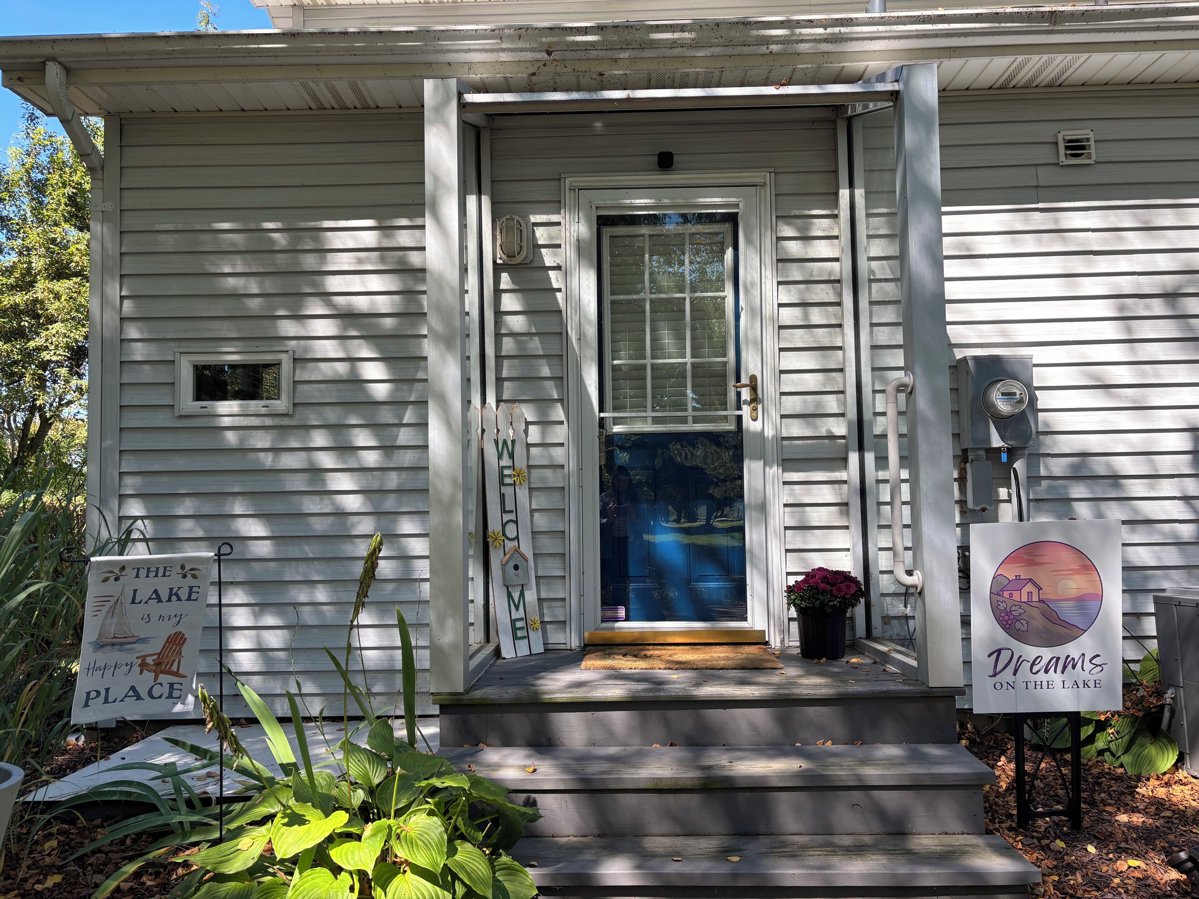 A white house with a front porch, a welcome sign, and a sign indicating it's a lake place.