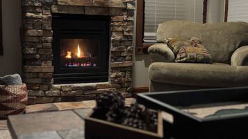 A stone fireplace with a fire, a sofa with a patterned cushion, and a woven basket on the floor.