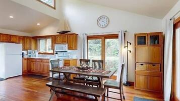 A spacious kitchen with wooden cabinets, a dining table with benches, a clock on the wall, and a view through the glass door.