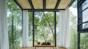 A room with tatami mats, a low table with a tea set, and a view of a forest through large windows. - Qingcheng Mountain Jiuxipo (Chengdu)