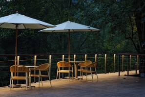 A deck with wooden chairs and tables, two white umbrellas, and a railing overlooking a forested area. - Qingcheng Mountain Jiuxipo (Chengdu)