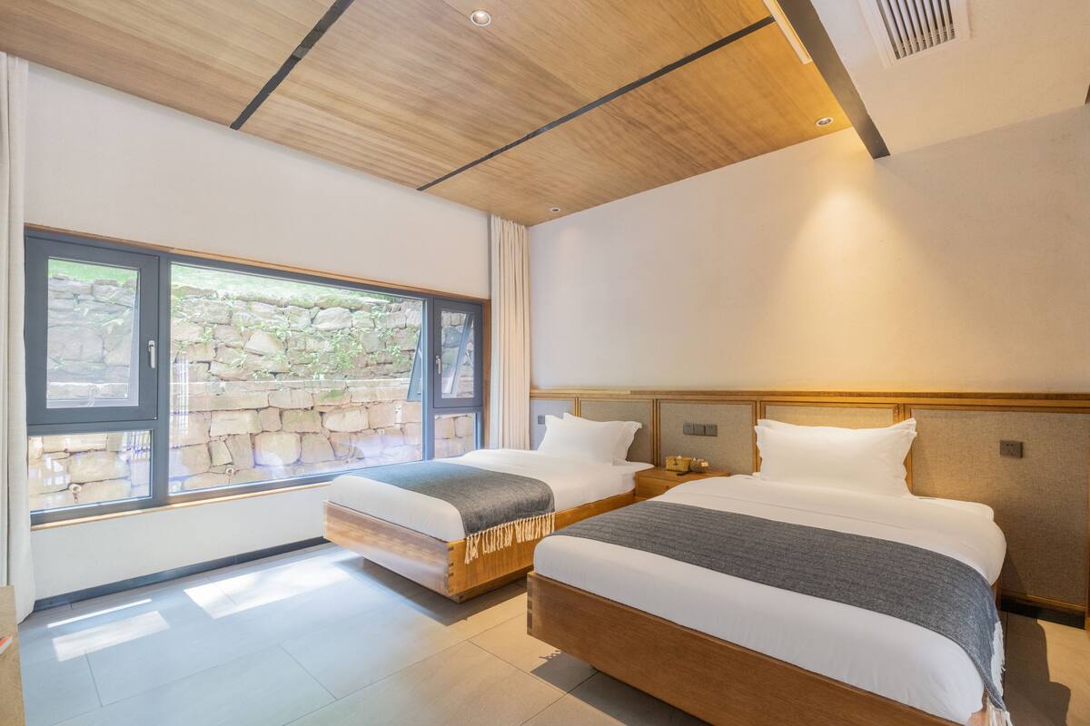 Habitación de hotel moderna con dos camas, vista a una pared de piedra y techo de madera.