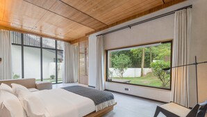 A modern bedroom with a large bed, a bedside table, and a chair. There is a window with curtains and a view of greenery outside. - Qingcheng Mountain Jiuxipo (Chengdu)