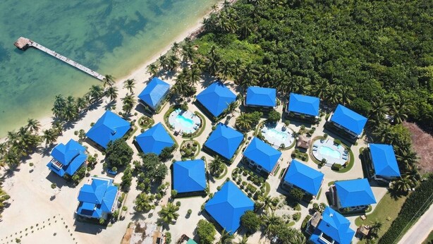 An aerial view of a resort with multiple blue-roofed buildings, a beach, and a pier extending into the water. - 4 BDRM Sunshine Suites @ Sapphire Beach Resort (Not available)