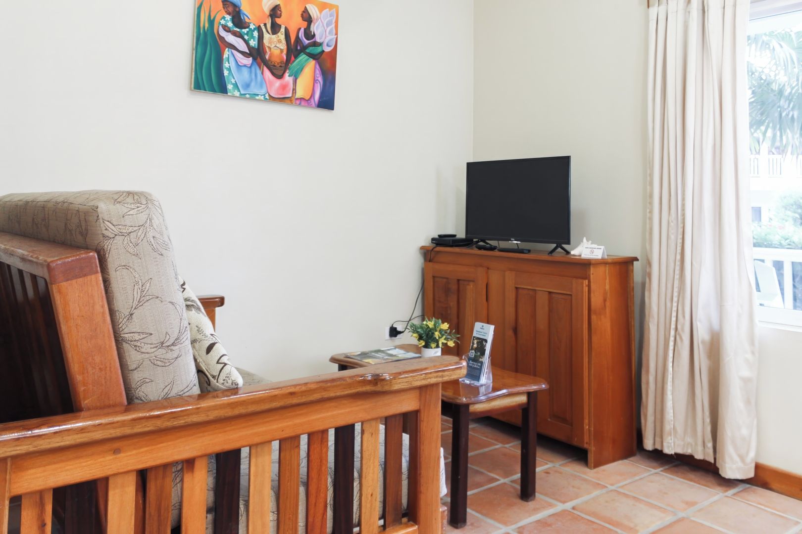 Un salon avec un canapé en bois, un téléviseur posé sur un meuble en bois et un tableau accroché au mur.