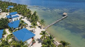 A coastal resort with multiple blue-roofed buildings, a pier extending into the sea, and a backdrop of palm trees and clear blue water. - 4 BDRM Sunshine Suites @ Sapphire Beach Resort (Not available)