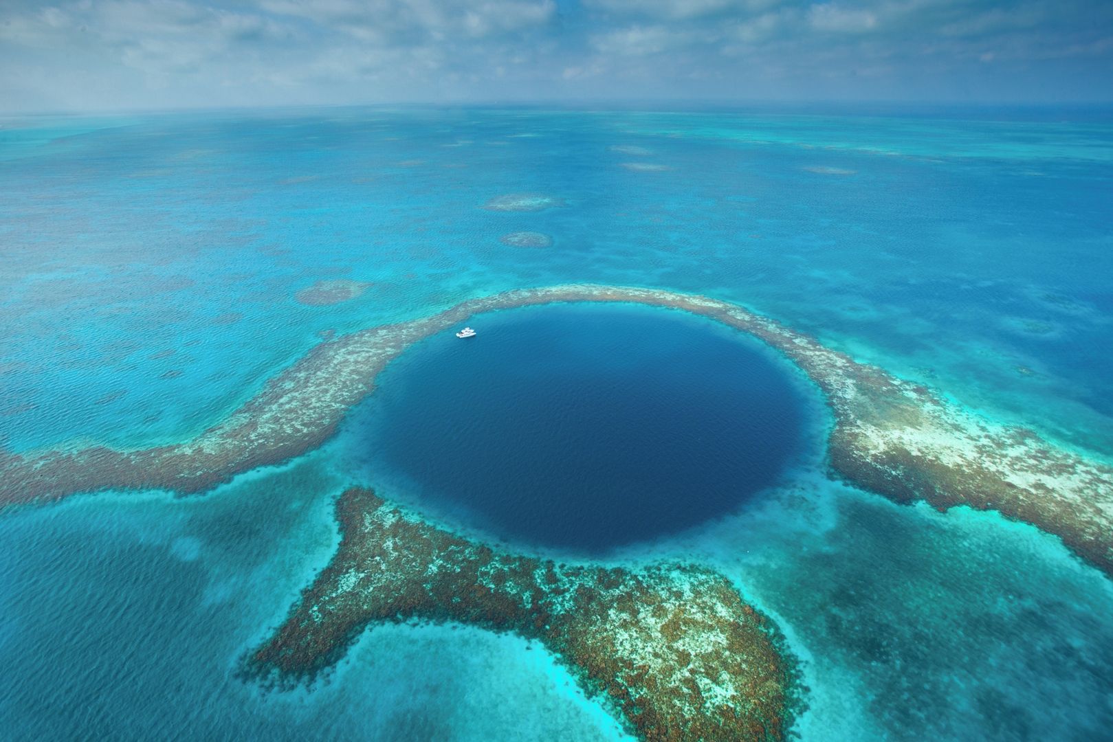 An aerial view of a large, circular, clear blue lagoon surrounded by coral reefs.