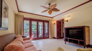 A living room with a sofa, a television, and a ceiling fan. - Tropical Tranquility Suite | Upper Level 1BR Sea (San Pedro)
