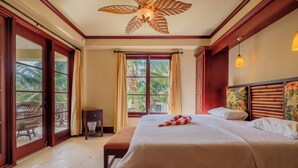 A spacious bedroom with a large bed, a ceiling fan, and a view of palm trees through the window. - Tropical Tranquility Suite | Upper Level 1BR Sea (San Pedro)