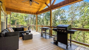 Een overdekt terras met een barbecue, tuinmeubilair en uitzicht op het bos.