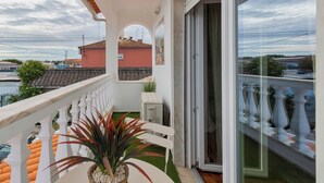 Un balcón con barandilla blanca, una planta en maceta y un ventanal corredero que da a una habitación.