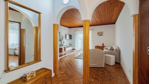 Una habitación amplia con suelo de madera, un espejo grande y un rincón de descanso acogedor con sofá y sillones.