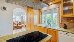 Una cocina con encimeras de granito, placa de cocción por inducción negra, armarios de madera, una ventana con vistas a zonas verdes y un comedor con mesa y sillas.