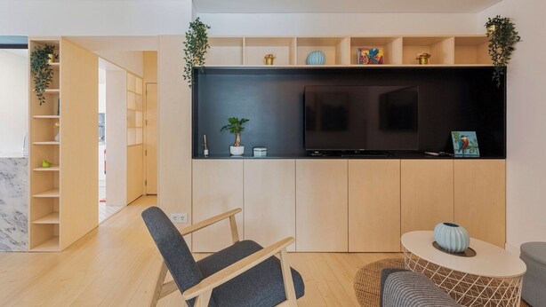 Une cuisine moderne dotée d’un grand téléviseur, de meubles en bois et d’un coin salon avec une chaise et une petite table.