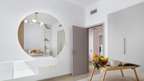 A modern room with a large round mirror, a wooden table with fruits and a cup, and a white wardrobe. - Maison Privee - Sleek Yas Getaway w/ Ferrari World and Canal Views (Abu Dhabi)