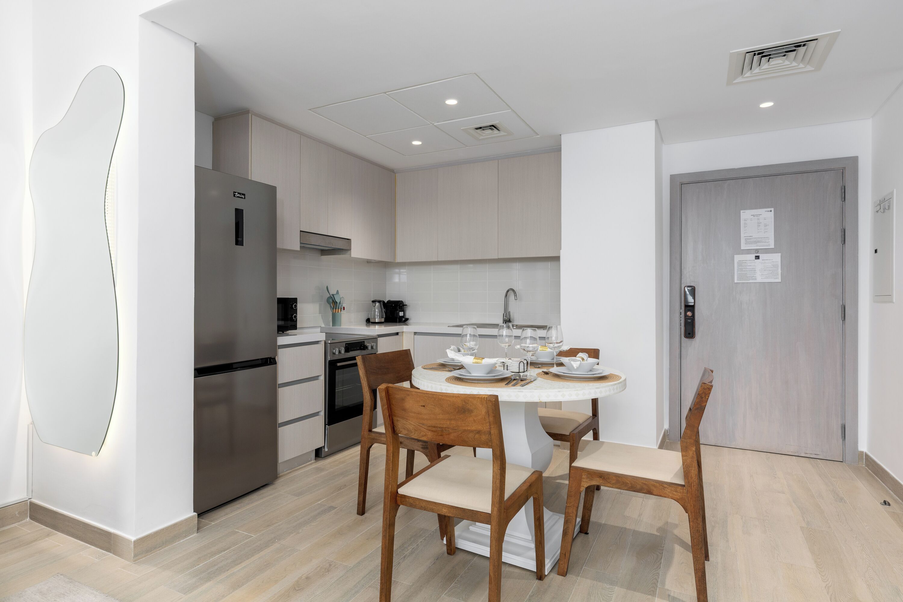 A modern kitchen with a built-in refrigerator, stove, and sink. There is a dining table with chairs and a white cabinet above it.