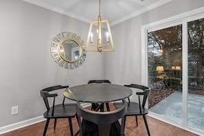 A dining area with a round table, four chairs, a chandelier, and a mirror on the wall.
