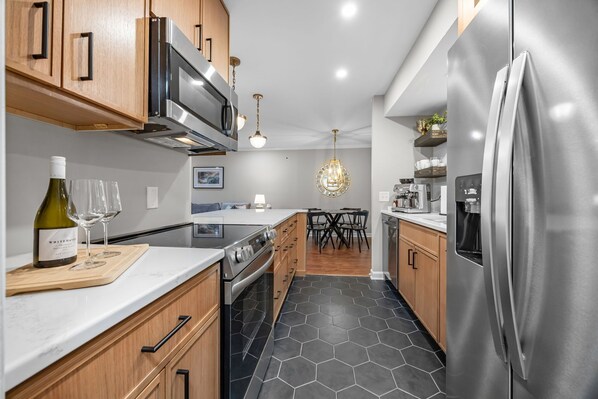 A modern kitchen with stainless steel appliances, wooden cabinets, and a hexagonal tile floor.