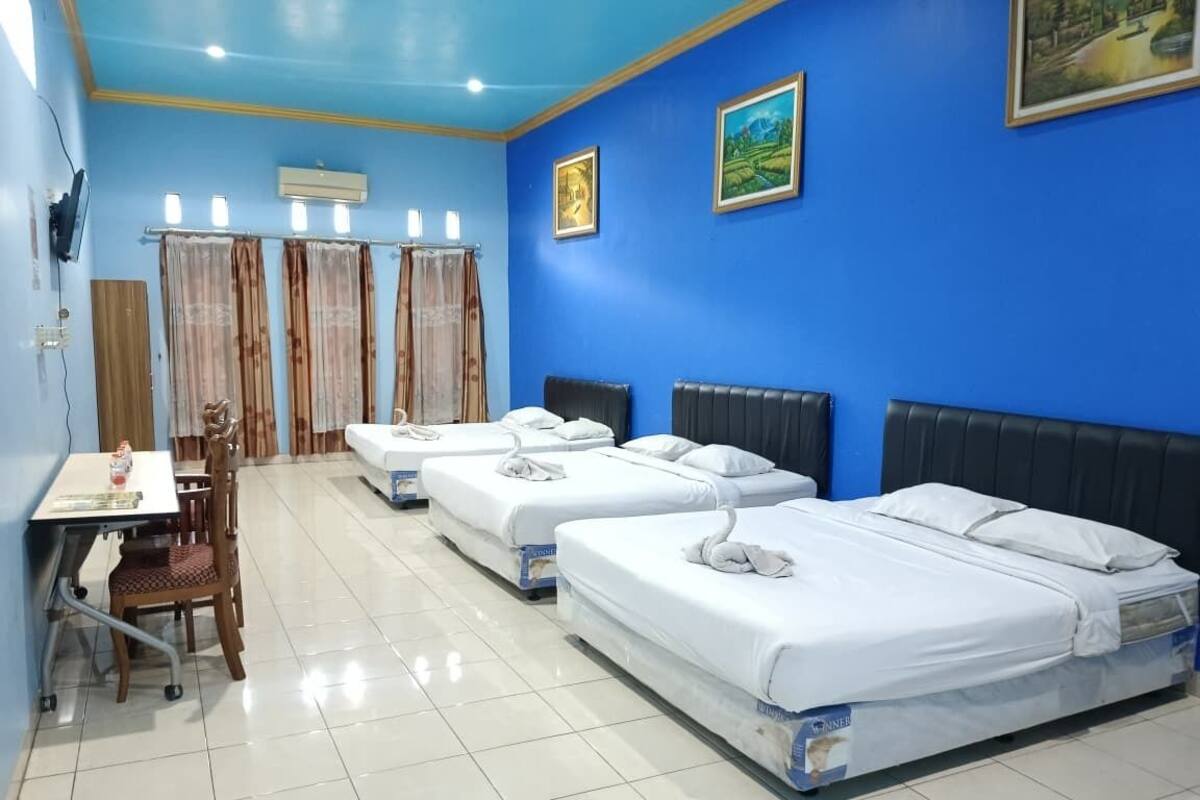 A hotel room with four single beds, a desk with a chair, and a window with curtains.