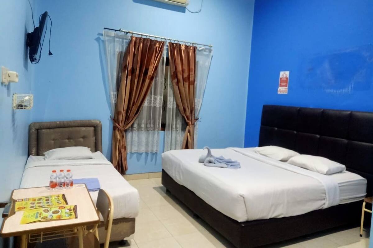 A hotel room with two beds, a small table with water bottles, a desk, and a window with curtains.