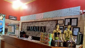 Un comptoir d’accueil sur lequel est affiché en grand le nom « AMALIA ». On y trouve deux mannequins vêtus de costumes traditionnels, et divers en-cas sont présentés sur le comptoir.