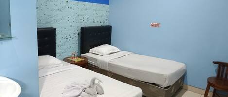 A hotel room with two single beds, a small table with a bottle, a chair, and a sink.