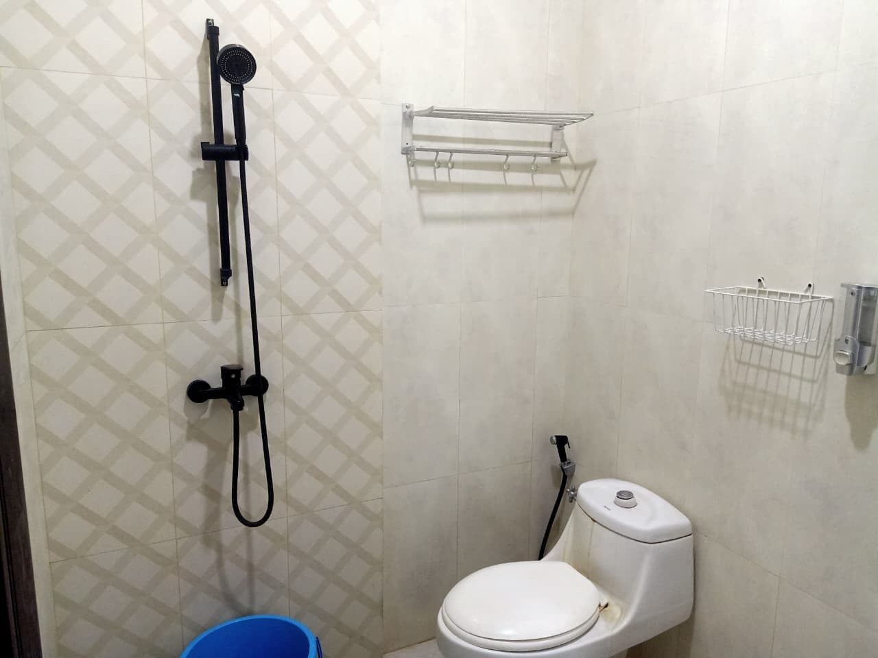 A small bathroom with a toilet, a shower, and a blue bucket.