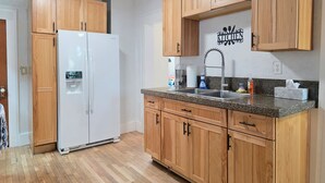 A kitchen with wooden cabinets, a white refrigerator, a granite countertop, and a stainless steel sink. - James Street Home Downtown Ludington (Ludington)