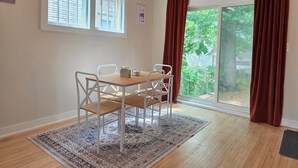 A dining area with a table and chairs, a patterned rug, and a view of a backyard through a sliding glass door. - James Street Home Downtown Ludington (Ludington)