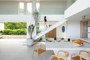 A modern interior with a staircase leading to an upper level, a dining area with a marble table, and a kitchen with wooden cabinets. - Bow Villa by Sublime Samui Villas (Koh Samui)