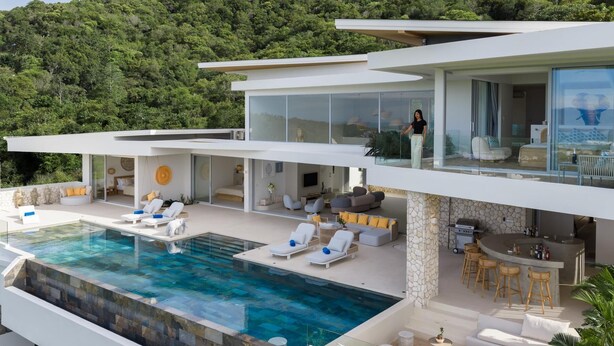 A modern multi-level house with a large outdoor pool, multiple seating areas, and a bar.