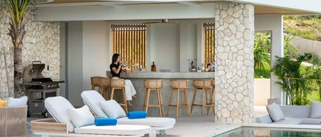 Un espace piscine extérieur moderne, doté de chaises longues, d’un bar et d’un barbecue.