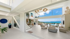 A spacious, modern interior with a high ceiling, a staircase leading to an upper level, and a large window offering a scenic view.